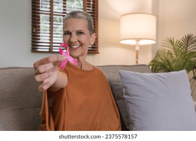 Portrait of confident smiling elderly senior woman with pink ribbon at her home. Health care, support, prevention. Breast cancer awareness month concept - Powered by Shutterstock