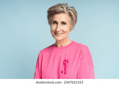 Portrait of confident smiling senior woman wearing pink t shirt with pink ribbon isolated on blue background. Health care, support, prevention. Breast cancer awareness month concept - Powered by Shutterstock