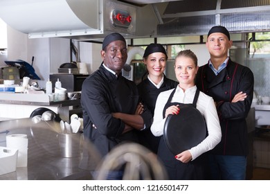 Portrait Of Confident Smiling Team Of Chefs In Interior Of Restaurant Kitchen 

