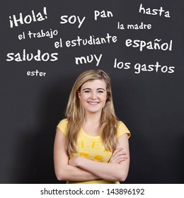 Portrait Of A Confident Smiling Teenage Girl With Arms Crossed Against Spanish Vocabulary On Black Background