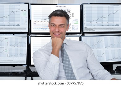 Portrait Of Confident Stock Market Broker Leaning On Desk At Office