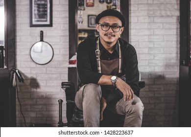 portrait of confident stylist man barber sitting at vintage barbershop chair with crossed arm facing and looking at camera