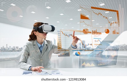 Portrait of confident and successful business woman in suit sitting inside office building with digital media interface and using virtual reality headset - Powered by Shutterstock