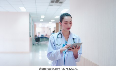 Portrait of Confident, successful professional Asian woman doctor in uniform white lab coat, stethoscope. Female physician work while stand using tablet corridor examination room in hospital medical.