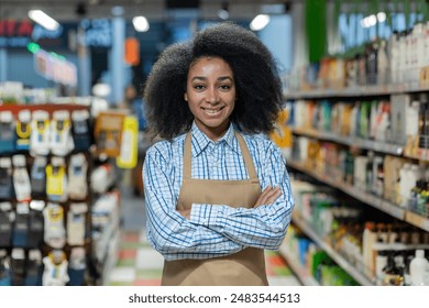 Portrait of a confident supermarket employee standing with crossed arms in an aisle. Wearing an apron and a friendly smile, she embodies professionalism and customer service in a retail environment. - Powered by Shutterstock