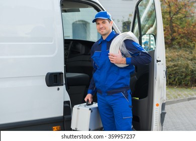 Portrait of confident technician with cable coil and toolbox standing outside van