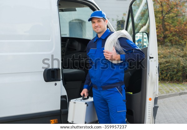 Portrait of confident technician with cable\
coil and toolbox standing outside\
van