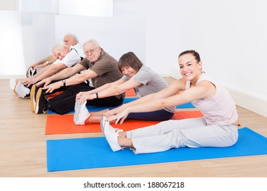 Portrait of confident trainer and customers doing stretching exercise at gym