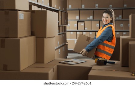 Portrait of a confident warehouse worker carrying a box, she is smiling at camera - Powered by Shutterstock