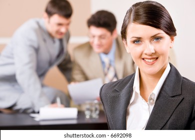 Portrait der selbstbewussten Frau mit bezauberndem Lächeln auf dem Hintergrund zweier Geschäftsmänner