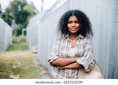 Portrait of a confident woman farmer in a checkered shirt and apron arms crossed holding a hat smiling in front of a farm's lush greenhouse tomatoes. Nature's beauty in a farming setting. - Powered by Shutterstock