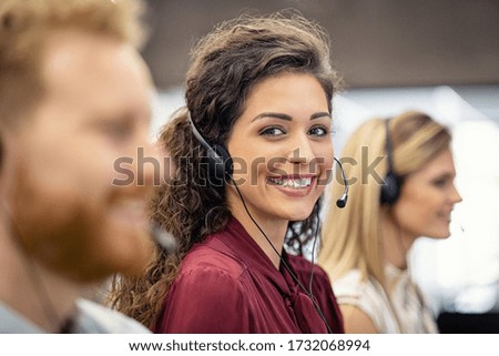 Portrait of confident woman working in a call center while looking at camera. Customer care rappresentative working with team in office sitting in a row. Support online with latin call center agent.