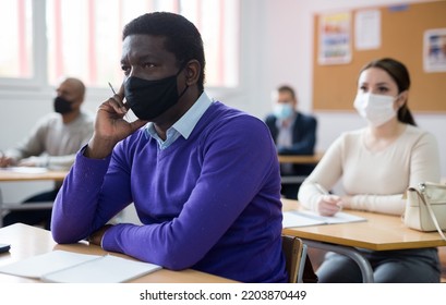 Portrait Of Confident Young Adult Male In Face Mask For Viral Protection Studying In Classroom With Colleagues