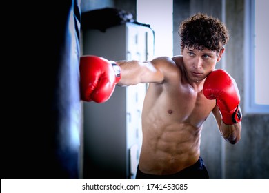 Portrait of a confident young athlete caucasian man in boxing gloves, punching A Bag in professioal gym. Sportsman muay thai boxer work out, training, fighting in gloves. - Powered by Shutterstock