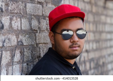 Portrait Of Confident Young Black Boy In Red Baseball Cap Posing At Grey Brick Wall With Graffiti On The Background.African Hip Hop Guy In Red Snap Back Baseball Hat,mirror Sunglasses