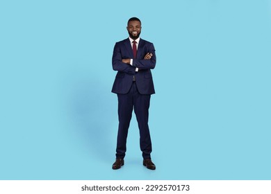 Portrait Of Confident Young Black Businessman In Suit Standing With Folded Arms, Handsome African American Male Entrepreneur Posing Over Blue Studio Background, Full Length, Copy Space - Powered by Shutterstock