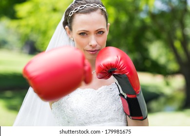 Portrait of confident young bride with boxing gloves punching in park - Powered by Shutterstock