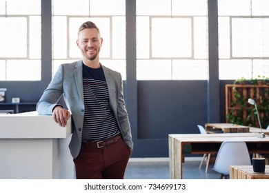 Portrait of a confident young businessman in a blazer smiling while standing by himself in a bright modern office