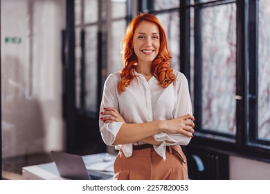 Portrait of confident young businesswoman standing in office with arms crossed. - Powered by Shutterstock