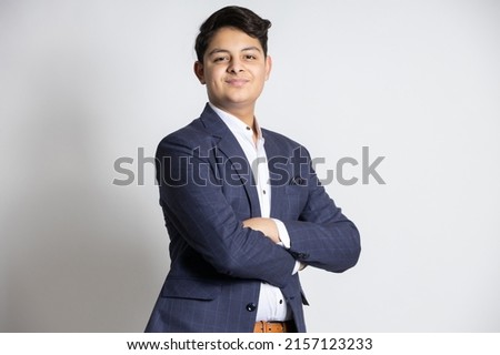 Portrait of a confident young indian teenager boy wearing suit standing with his arms cross, isolated on white studio background.