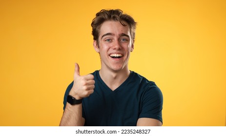 Portrait of confident young man 20s with smiling crossing arms nod head yes, giving thumbs up, posing isolated on yellow background studio. People lifestyle emotions concept.