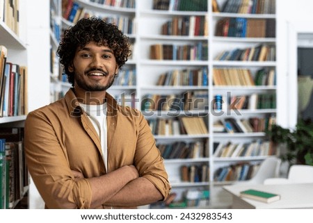A portrait of a confident young man standing with his arms crossed in a well-stocked library. The image conveys a sense of knowledge, education, and self-assurance amid a backdrop of bookshelves