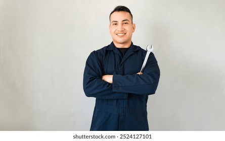 Portrait of a confident young mechanic holding a wrench and smiling against a gray background - Powered by Shutterstock