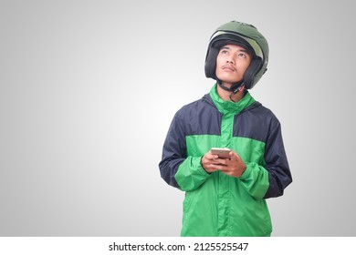 Portrait Of Confused Asian Online Taxi Driver Wearing Green Jacket And Helmet Thinking About An Idea And Looking Up. Isolated Image On White Background