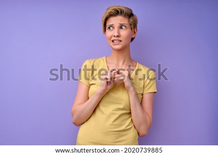 Portrait of confused caucasian attractive short haired female feeling awkward, looking aside with weird smile after making mistake and being guilty, saying oops over purple background, copy space