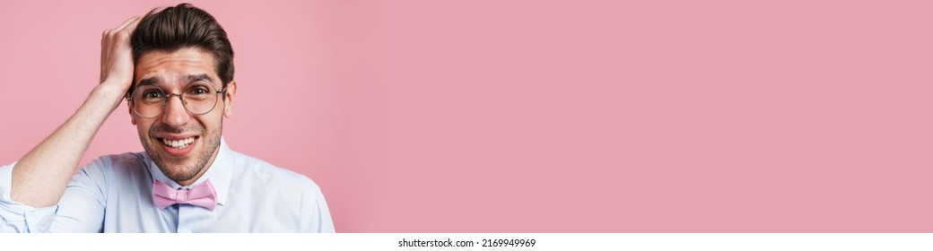 Portrait Of A Confused Frowning Young Brunette Nerd Man Wearing Shirt And Bowtie Standing Over Pink Wall Background