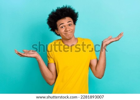 Portrait of confused funny guy afro hairdo wear yellow t-shirt shrugging shoulders has no idea isolated on shine teal color background