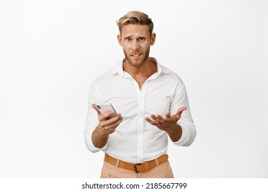 Portrait Of Confused Man Holding Cellphone With Clueless Face Expression, Dont Understand, Standing Against White Background