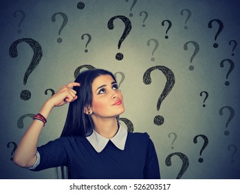 Portrait confused thinking young woman bewildered scratching head seeks a solution looking up at many question marks isolated on gray wall background. Human face expression