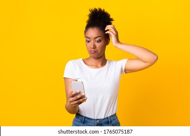 Portrait Of Confused Young African Woman Using Mobile Phone, Scratching Head, Posing Isolated Over Yellow Studio Wall