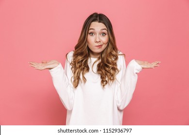 Portrait of a confused young casual girl shrugging shoulders isolated over pink background - Shutterstock ID 1152936797