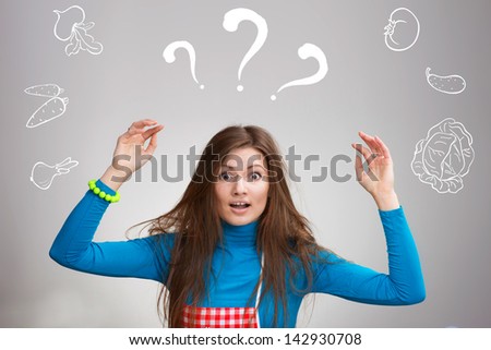 Portrait of a confused young housewife with the drawn vegetables on grey background