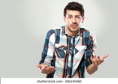 portrait of confused young man shrugging his shoulders posing next to color background