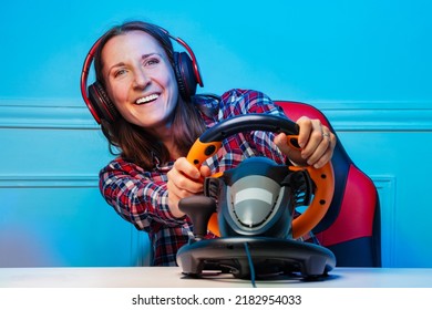 Portrait with console steering wheel of a laughing happy gamer woman in headphones playing race game