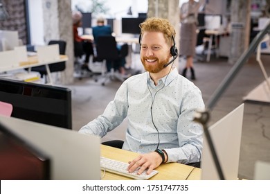 Portrait Of Consultant Agent Man In Call Center Smiling. Happy Customer Support Agent Working With Headset While Sitting At His Workstation. Smiling Telephone Operator Using Computer In Open Office.