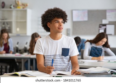 Portrait of contemplative young man during exam at high school. Smiling college student doing homework in class while looking away. Pensive african young man preparing for exam in university classroom