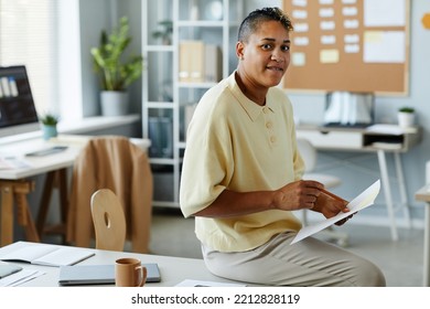 Portrait Of Contemporary Black Woman With Short Hair Sitting On Desk In Casual Office Setting And Looking At Camera , Copy Space