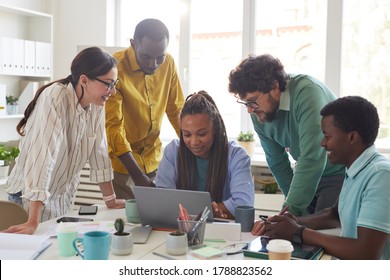 Portrait of contemporary multi-ethnic team leaning over laptop and smiling while working together in office, copy space