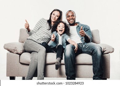 Portrait of content mother, father and daughter relaxing on sofa and showing thumbs. Isolated on background - Shutterstock ID 1023284923