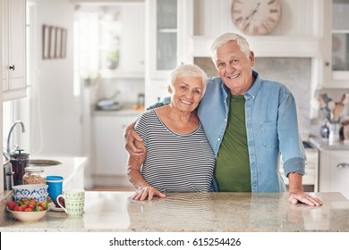 Portrait of a content senior man with his arm around his wife's shoulder standing together in their  kitchen at home