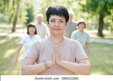 Portrait Of Content Serene Mature Yoga Instructor Making Namaste Gesture While Standing In Front Of Her Students In Park