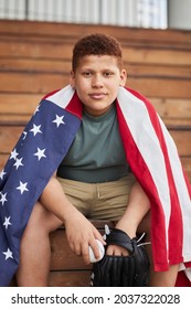 Portrait Of Content Teenage African American Baseball Player In Black Glove Sitting On Bench And Holding Ball