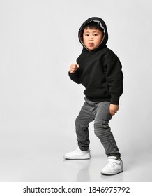 Portrait Of A Cool Asian Boy In A Black Hoodie With A Hood, Jeans And White Sneakers Standing On A White Background. Concept For Sport And Healthy Activity For Modern Kid. Place For Text.