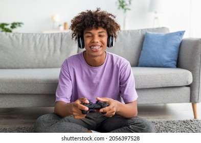 Portrait Of Cool Black Teen Gamer With Controller Playing Online Video Games, Wearing Headphones At Home. African American Adolescent Having Fun Hobby During Covid Quarantine, Indoors