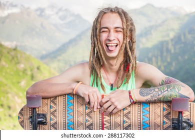 Portrait of cool, funny handsome man with skateboard outdoor at mountain. Real guy with strong character and personality. He is ready for World Day of skateboarding
