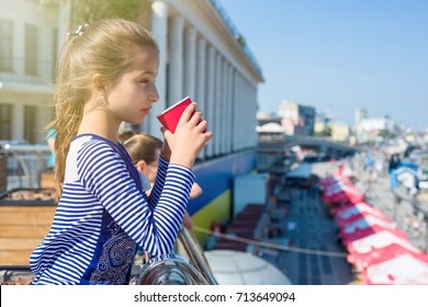 Portrait Of A Cool Girl 10 Years Old, In Profile, Drinks From A Glass And Looks Afar On The River. City Embankment, European City